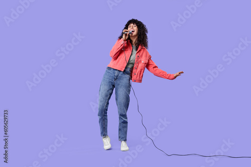 Beautiful young woman with microphone singing on purple background