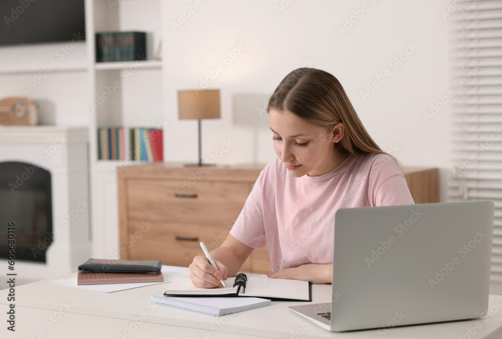 Online learning. Teenage girl writing in notepad near laptop at table