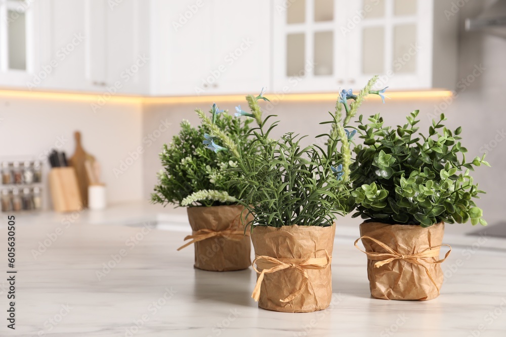 Artificial potted herbs on white marble table in kitchen, space for text. Home decor