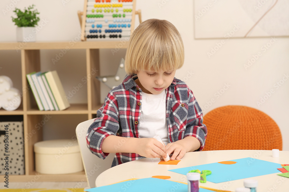 Cute little boy using glue stick at desk in room. Home workplace Cute little boy using glue stick at desk in room. Home workplace
