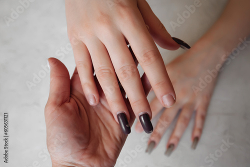 the manicurist holds the hand of a client with untidy broken nails  with an overgrown manicure to update