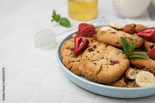 Cookies with freeze dried fruits  mint and nuts on white tiled table  closeup. Space for text