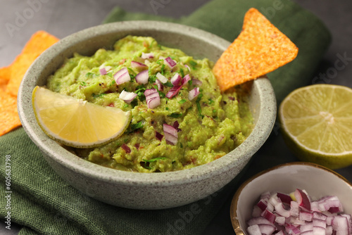 Bowl of delicious guacamole, nachos chips and lime on table, closeup