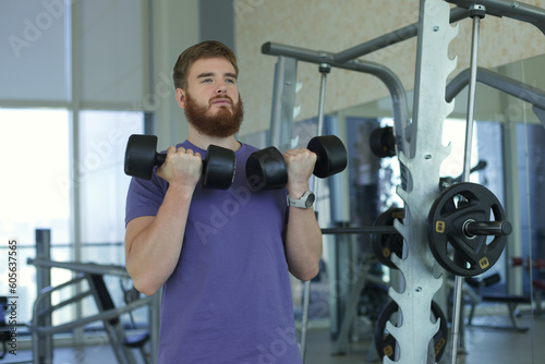 Bearded young man training in the gym with dumbbells 