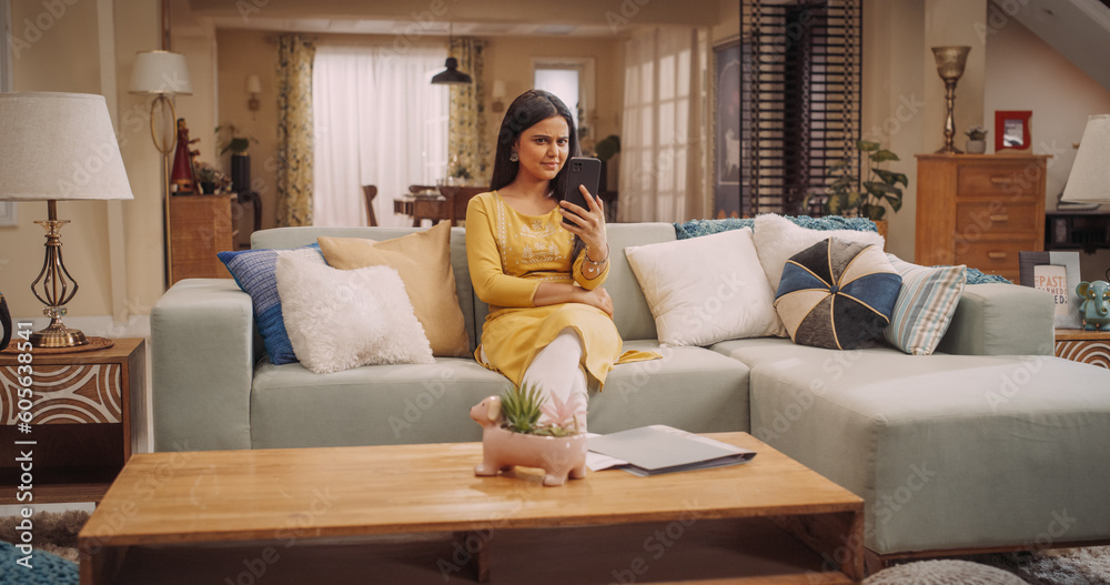 Portrait of a Confused Young Indian Woman Looking at her Smartphone, Reading the News in her Fancy Home. Surprised Girl Reacting to Prices and Sales on Online Shops, Reading Gossip Messages Portrait of a Confused Young Indian Woman Looking at her Smartphone, Reading the News in her Fancy Home. Surprised Girl Reacting to Prices and Sales on Online Shops, Reading Gossip Messages