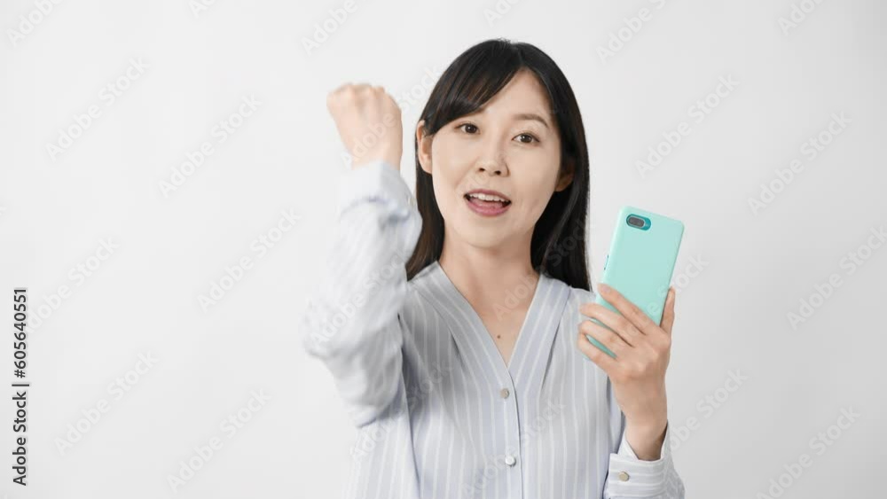 スマートフォンを持ちながらガッツポーズをする若い女性 スマートフォンを持ちながらガッツポーズをする若い女性