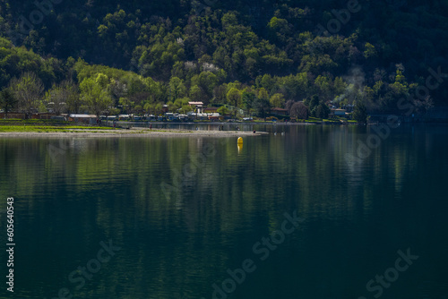 Lake Lugano surrounded by mountains and a small marina with moored boats on a sunny day