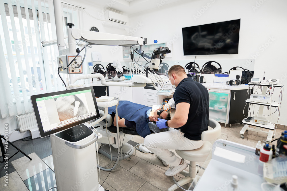 Dentist making X-ray, examining, inspecting problem, disease, holding equipment. Male doctor sitting on chair, fixing teeth, looking at screen. Concept of stomatology. Dentist making X-ray, examining, inspecting problem, disease, holding equipment. Male doctor sitting on chair, fixing teeth, looking at screen. Concept of stomatology.