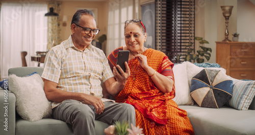 Elderly Couple Using Smartphone for Video Call at Home: Connecting with Loved Ones, Sharing Life's Moments, and Creating Lasting Memories. Embracing Technology to Stay Close. Medium Shot.