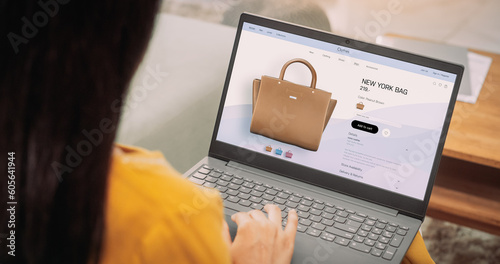 Over-the-Shoulder: Woman Using Laptop to Buy a Bag: Female Browsing through Internet, Doing Online Shopping, Comparing Prices for Items on Sale on a Retail Brand Website. E-commerce Concept photo