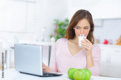 woman checking her laptop while drinking milk