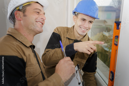 two builders holding spirit level against window and laughing