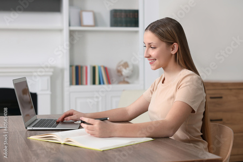 Online learning. Teenage girl writing in notebook near laptop at home