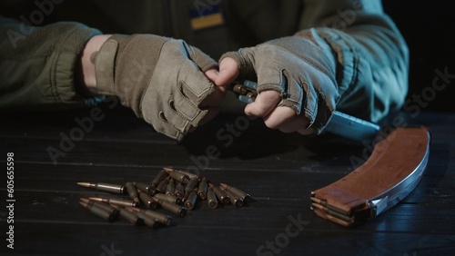 The male hands of a Ukrainian military man load a kalashnikov assault rifle magazine with cartridges close up. War in Ukraine. Russian aggression and military invasion of Ukraine.