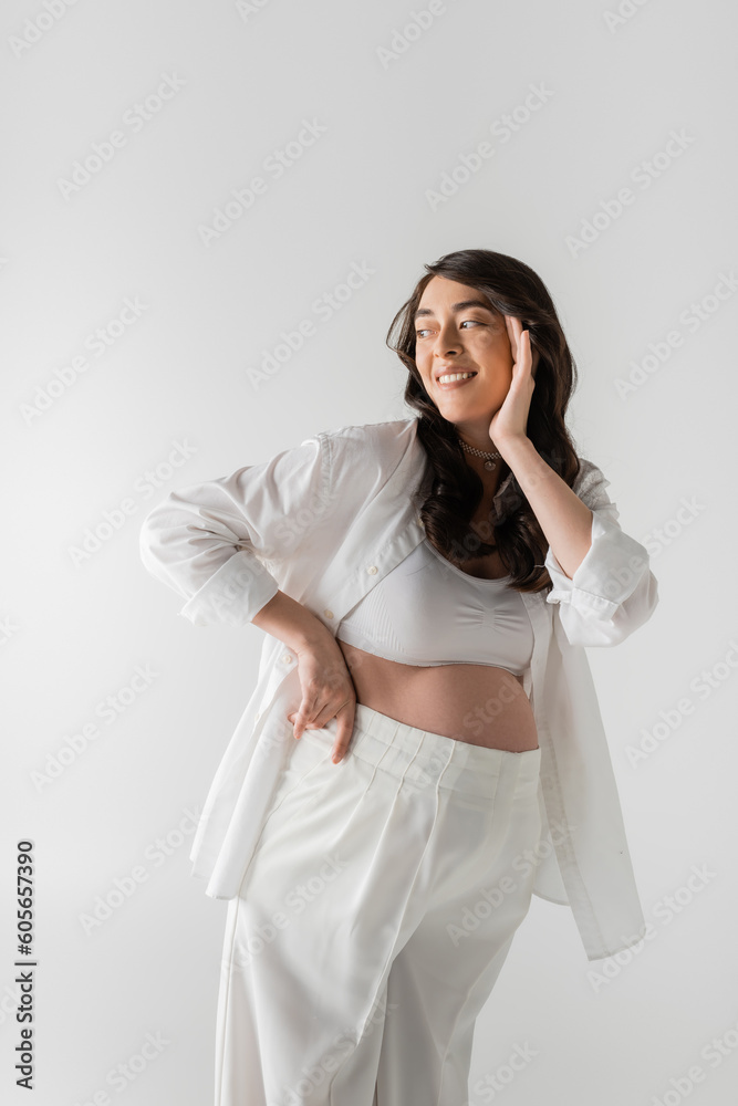stylish and charming pregnant woman in white crop top, stylish shirt and pants touching happy face and looking away isolated on grey background, maternity fashion concept stylish and charming pregnant woman in white crop top, stylish shirt and pants touching happy face and looking away isolated on grey background, maternity fashion concept