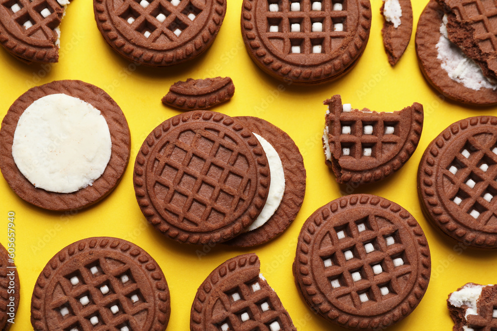 Tasty chocolate sandwich cookies with cream on yellow background, flat lay