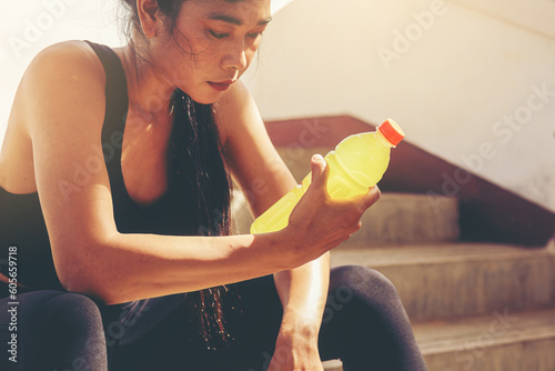 Tired runner woman with a bottle of electrolyte drink freshness after training outdoor workout at the stadium stairway. photo