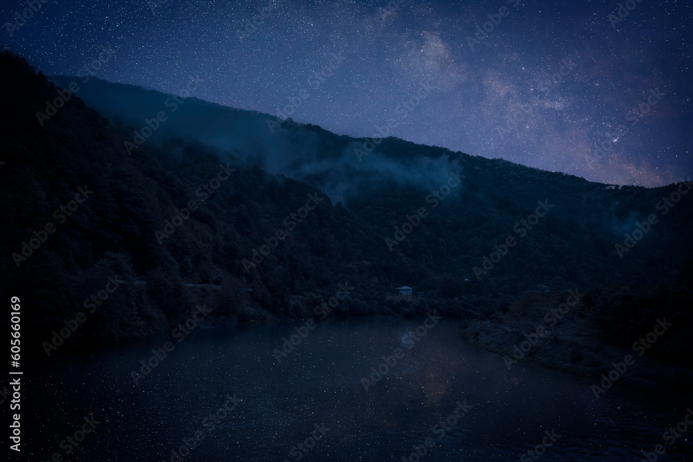 Lake with reflection of starry sky near mountains. Amazing night landscape