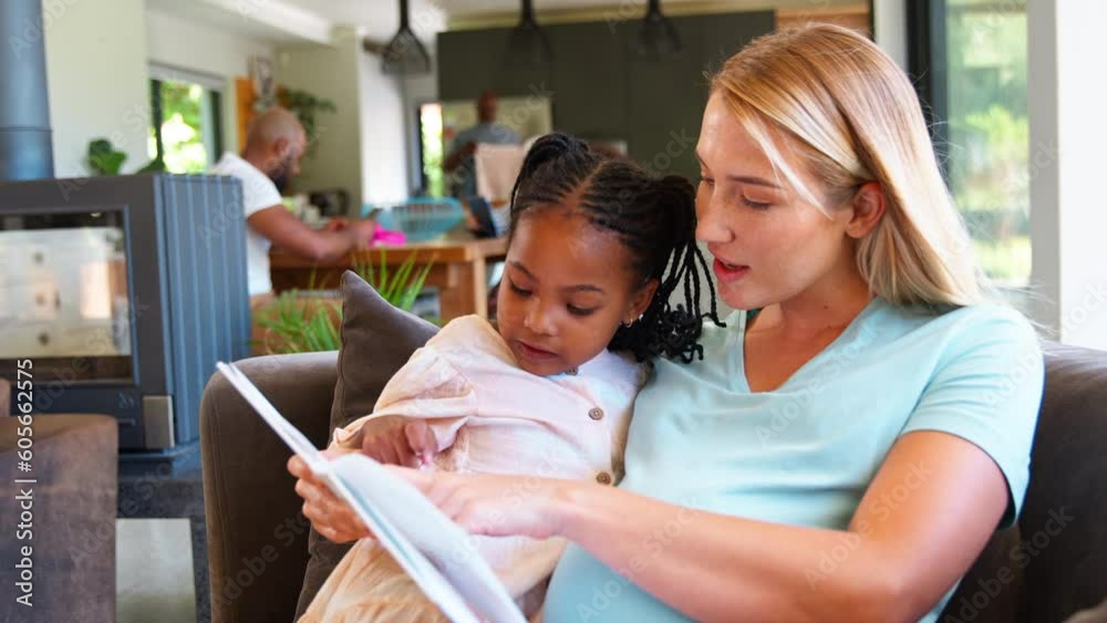 Pregnant mother and daughter reading book at home together with family in background - shot in slow motion Pregnant mother and daughter reading book at home together with family in background - shot in slow motion