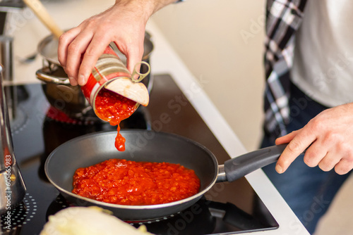 Man cooking at home kitchenn adding sauce to pan.
