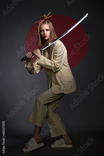 a beautiful girl with a beautiful figure in a light suit and a Japanese sword in her hands pose standing in the studio on a dark background