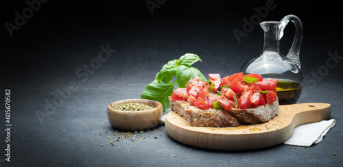 Tomato bruschetta with extra virgin olive oil, fresh basil and oregano on abstract dark gray background, space for text.