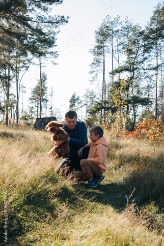 Dad with his son and a small brown dog are playing in a meadow with tall grass. Family leisure with a pet in nature. Front view
