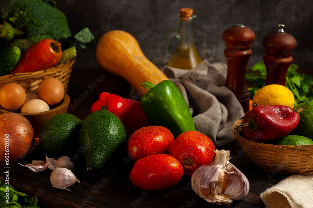 still life photo of various vegetables on a wooden table with vegetables in a wicker basket with oil and pepper shakers.