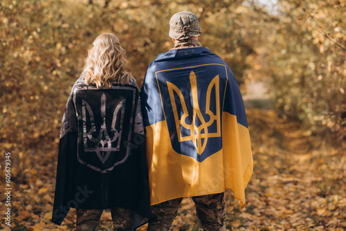 A Ukrainian military couple, embracing, with a Ukrainian flag on their backs.