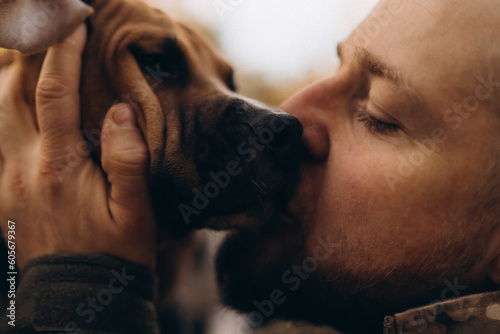 A soldier with a dog on the street on a sunny day. He hugs and kisses the dog.