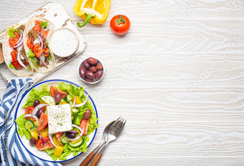 Traditional Greek Food: Greek Salad, Gyros with meat and vegetables, Tzatziki sauce, Olives on White rustic wooden table background from above. Cuisine of Greece. Copy space