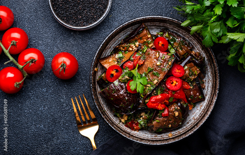 Grilled eggplant with red chili peppers, parsley, sesame seed, soy sauce and garlic in asian style, black table background, top view