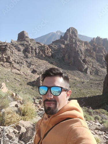 hipster guy with sunglasses on Teide Tenerife canary island. Positive traveler boy with goggles enjoying alone on a journey in a volcano valley like mars. Looking making selfie on lava land