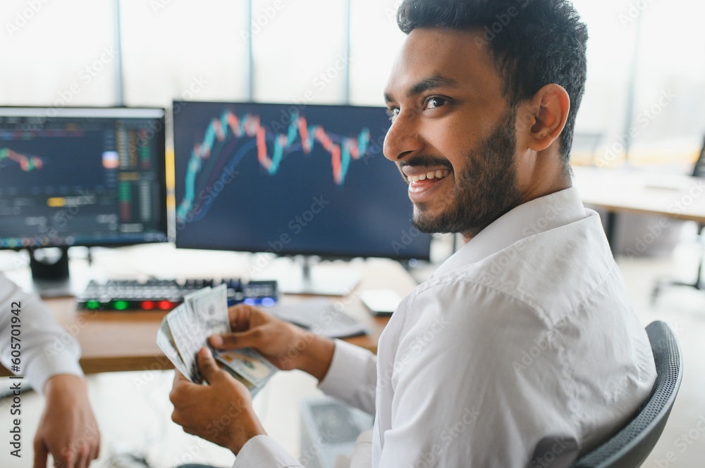 Fototapeta premium Portrait of a positive successful Indian or Arabian trader, stock market broker, Crypto charts on laptop screen