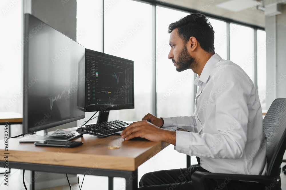 Side view of smart Indian crypto trader, investor, analyst broker, using laptop and smartphone analyzing digital cryptocurrency exchange, stock market charts, thinking of investing and funds risks. Side view of smart Indian crypto trader, investor, analyst broker, using laptop and smartphone analyzing digital cryptocurrency exchange, stock market charts, thinking of investing and funds risks.