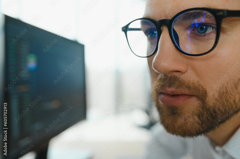 Young business man trader wearing glasses looking at computer screen with trading charts reflecting in eyeglasses watching stock trading market financial data growth concept, close up. Young business man trader wearing glasses looking at computer screen with trading charts reflecting in eyeglasses watching stock trading market financial data growth concept, close up.