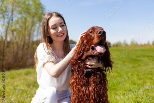 girl petting brown dog breed Irish setter outdoors in the park, woman walks with pet in the summer on the lawn