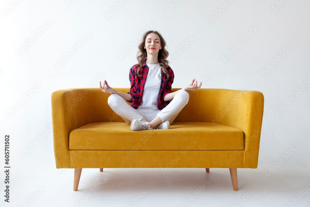 young cute girl sits in lotus position on soft comfortable sofa and meditates, woman does yoga on yellow couch young cute girl sits in lotus position on soft comfortable sofa and meditates, woman does yoga on yellow couch