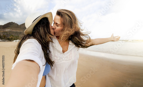 Happy gay lesbian couple kissing at the beach - Lgbt women taking selfie picture with mobile phone outside - Summer travel lifestyle concept