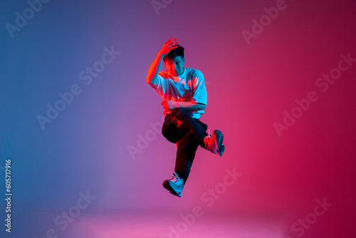 male dancer jumps and flies in the air, young guy hiphop performer break dances in neon club lighting