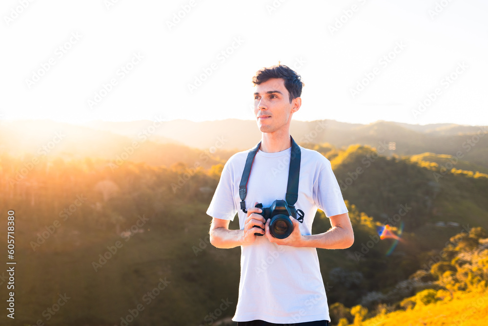 Portrait of a traveling photographer standing on top of a mountain while holding his digital camera with the sunset in the background. Portrait of a traveling photographer standing on top of a mountain while holding his digital camera with the sunset in the background.