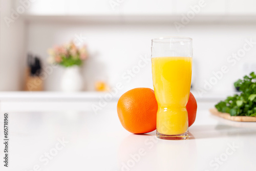 freshly squeezed orange juice in a glass stands near oranges in white modern kitchen, healthy food and drinks