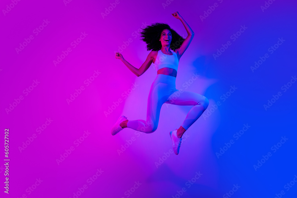 Full length photo of slim funny person jumping raise fists empty space ad leggings top shoes isolated on colorful neon background