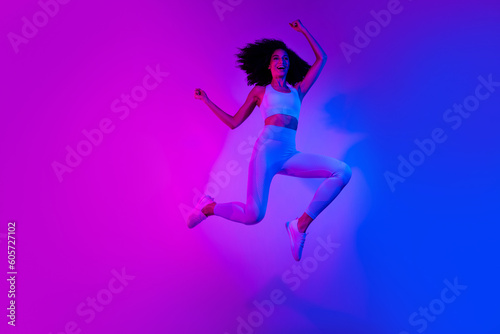 Full length photo of slim funny person jumping raise fists empty space ad leggings top shoes isolated on colorful neon background