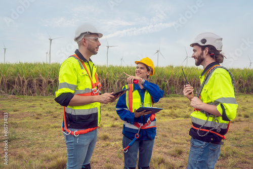 Two male engineers and a female foreman in safety jackets team talk plan work to inspect and repair wind turbines to wind power produce electricity in the turbine field.