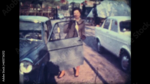 A smiling young woman gets into a light blue and blue fiat 1100 car and then walks with her husband through a park year 1964