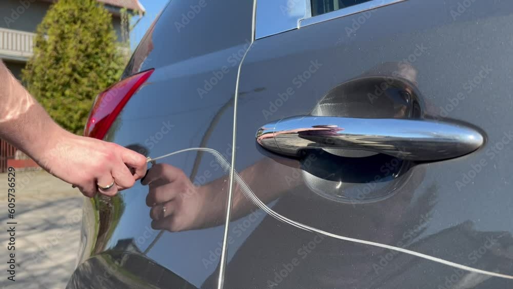 Man hand scratching a car body surface with a key. Devastation, destroying an expensive car on purpose.