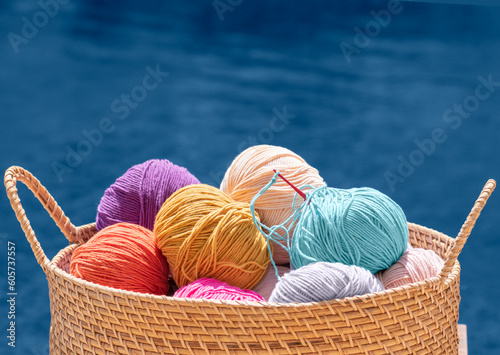 Knitting, crochet, needlework. Still life photo with multicolored wool skeins of yarn in basket isolated on blue background, close up. Hobby, relaxation, diy, handicraft during summer holidays