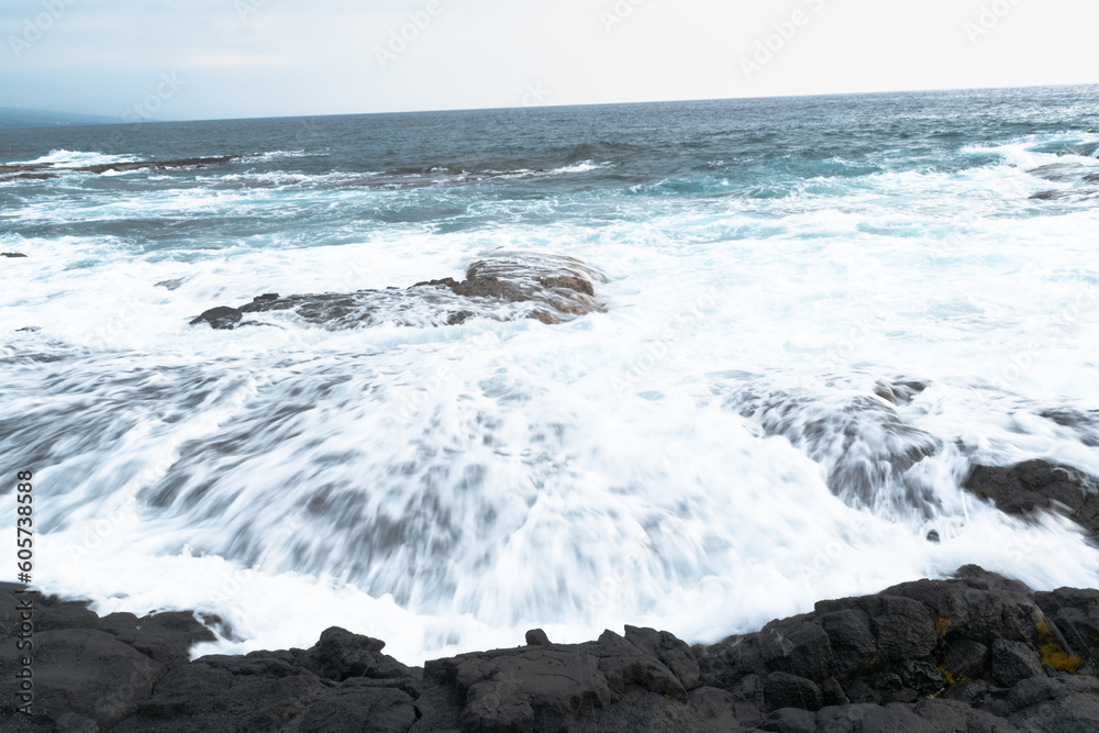 A person standing on a rock looking at waves coming up into the ocean. A person standing on a rock looking at waves coming up into the ocean.