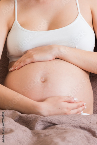 Young pretty pregnant woman, in pain, sitting on bed in bedroom, preparing to give a birth